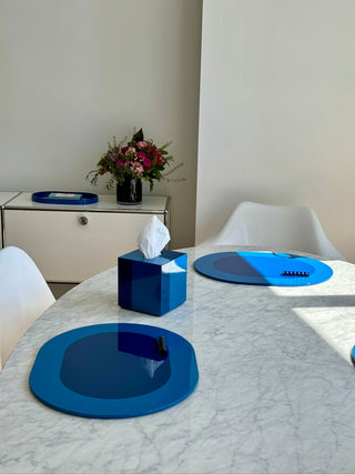 Two Rhapsody Blue lacquer placemats and tissue case on a marble dining table